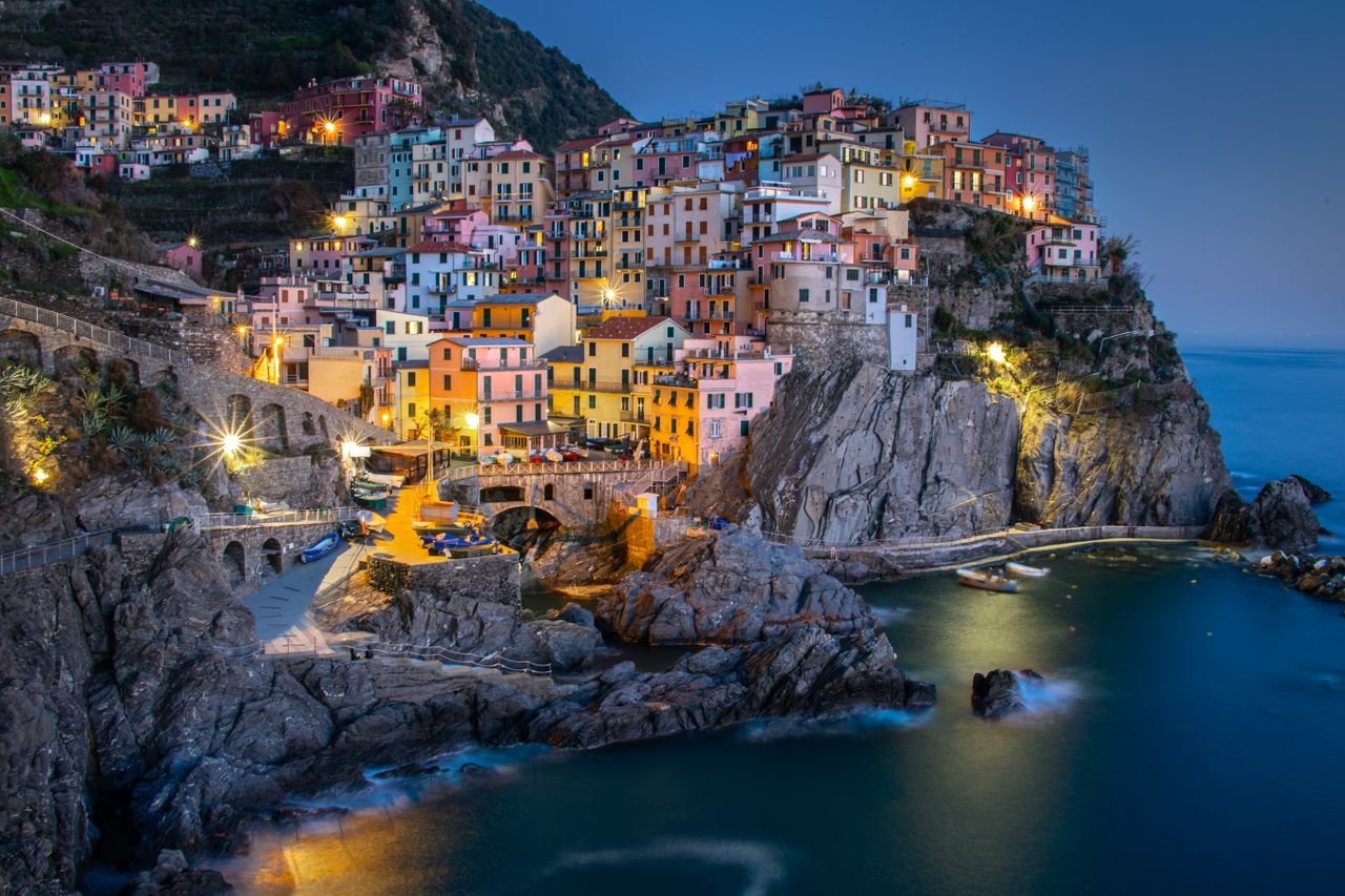 Colorful evening view of Manarola village, Cinque Terre, Italy, with illuminated houses overlooking the sea.