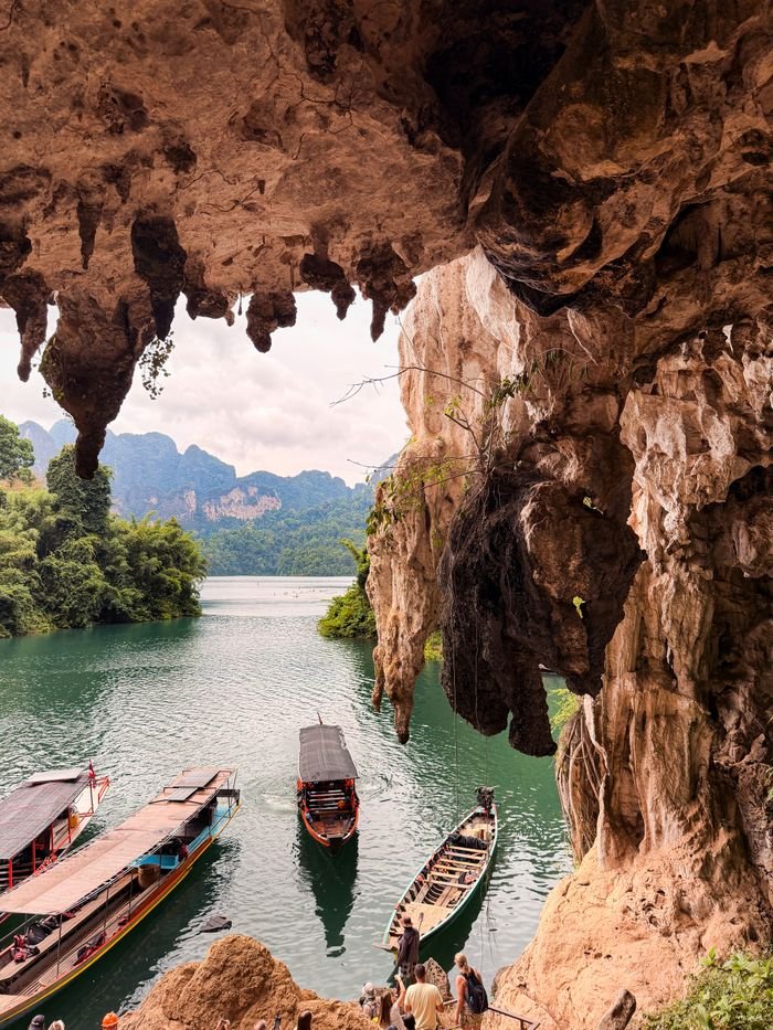 Explore stunning cave formations overlooking boats on a tranquil tropical lake.