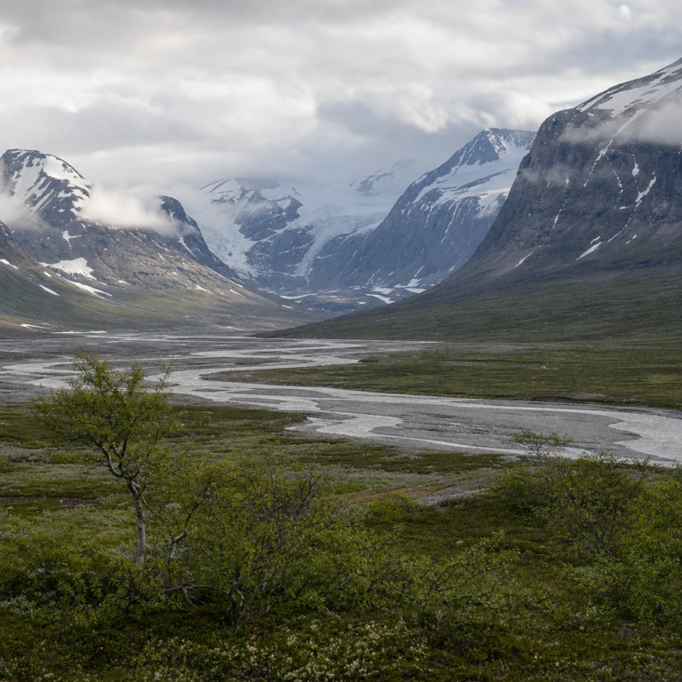 Wide Arctic mountain valley with a braided glacial river, glaciers on snow-streaked peaks and low cloud